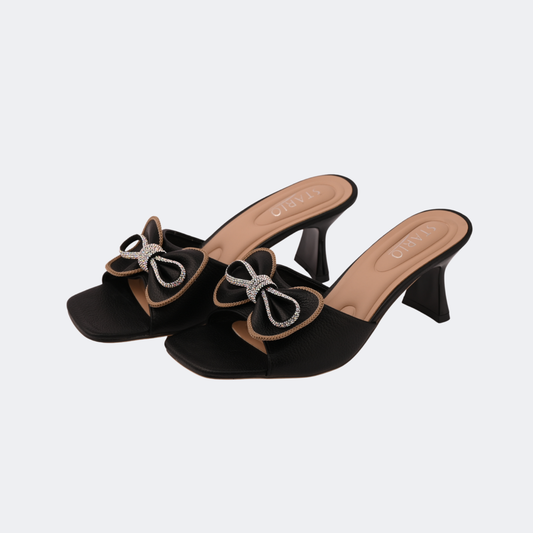 Black high-heeled shoes with decorative bows on a light gray background | Vogelle