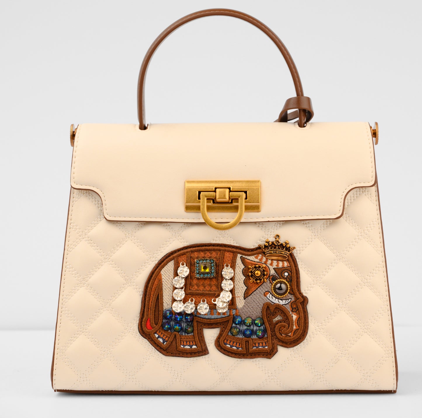 Beige handbag with a decorative lion emblem featuring jewelry on a light gray background | Vogelle