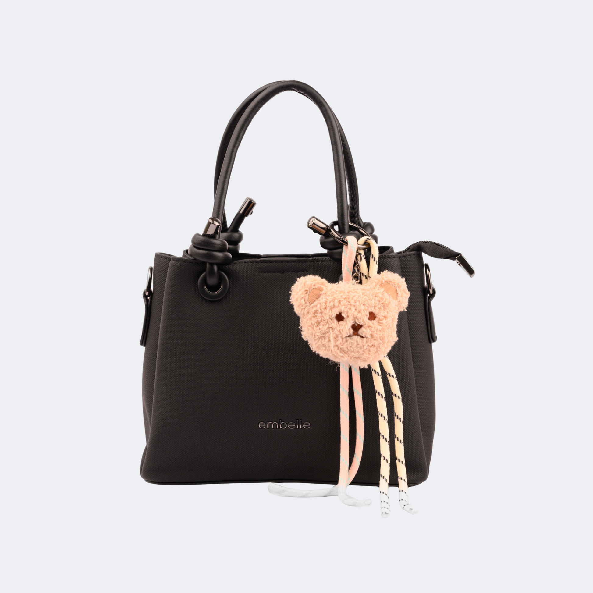 Black handbag with a teddy bear keychain on a light gray background | Vogelle