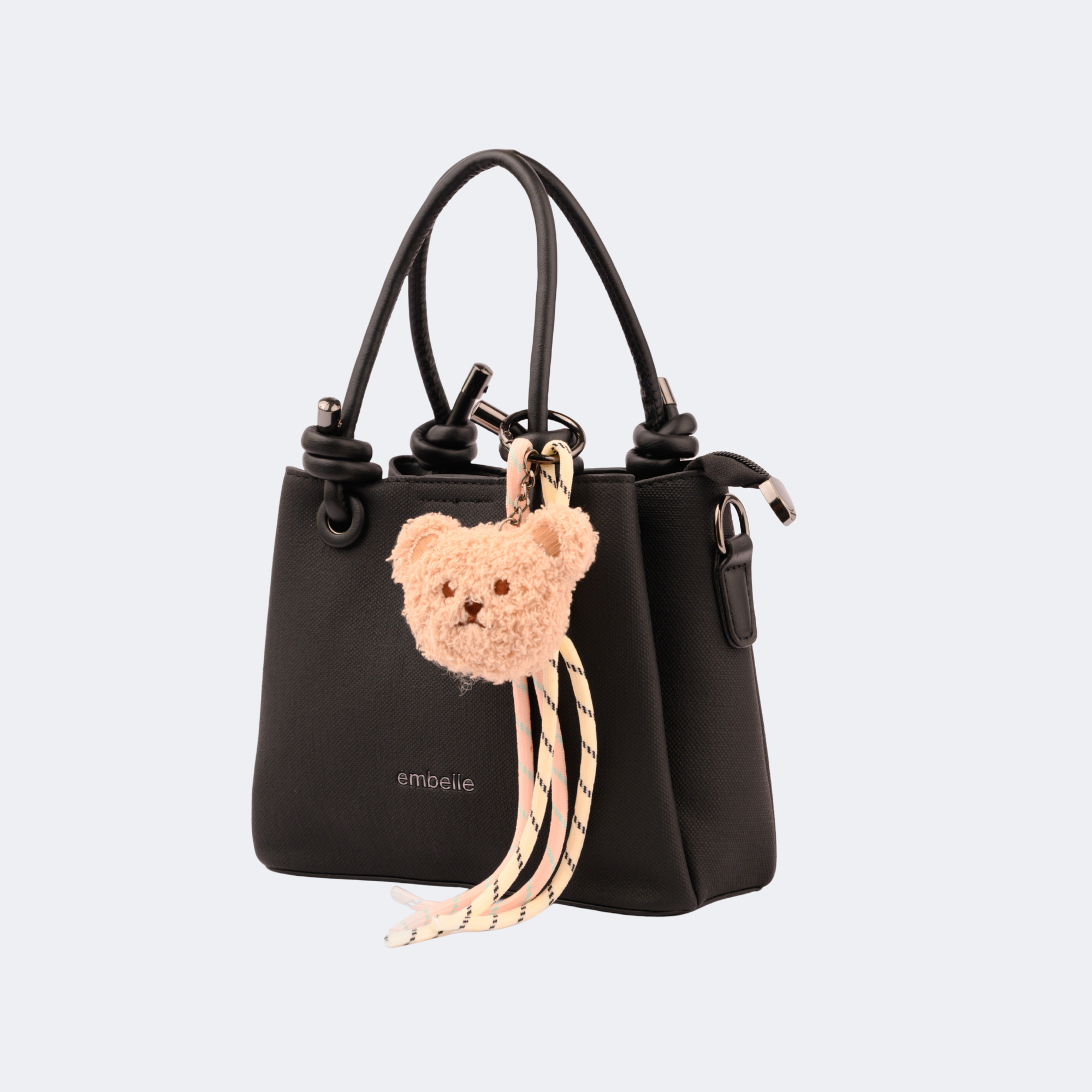 Black handbag with a teddy bear keychain on a light gray background | Vogelle