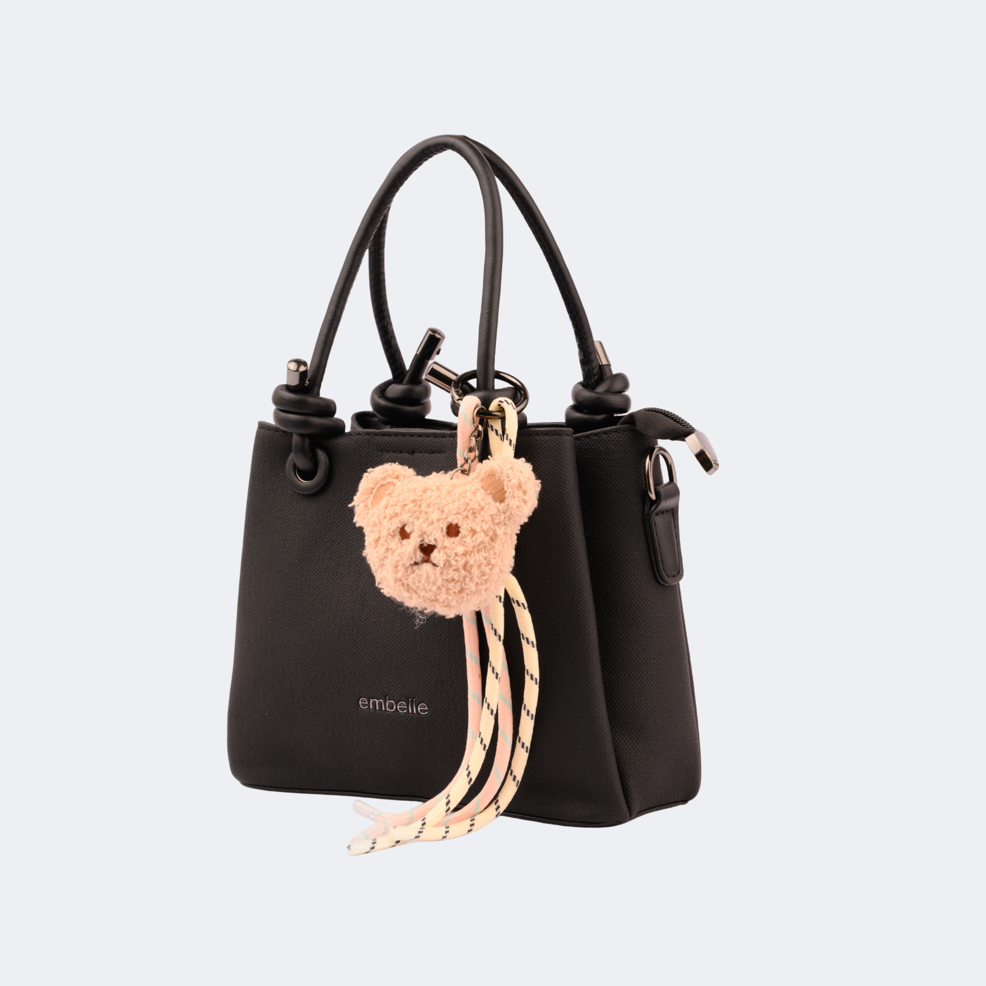 Black handbag with a teddy bear keychain on a light gray background | Vogelle