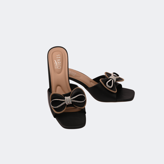 Black sandals with bow details on a light gray background | Vogelle