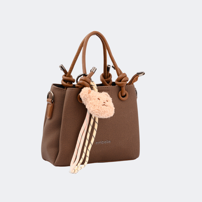 Brown handbag with a decorative keychain on a light gray background | Vogelle