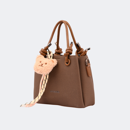 Brown handbag with a teddy bear charm on a light gray background | Vogelle
