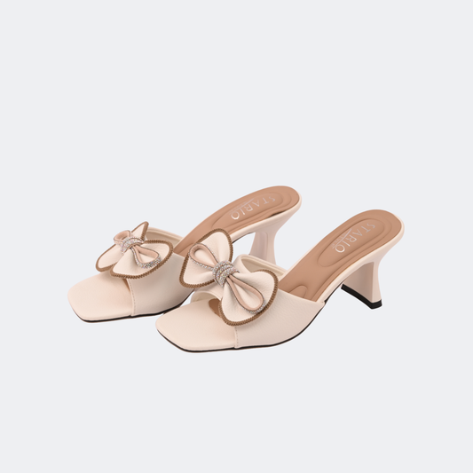 Pair of beige high-heeled shoes with bow details on a light gray background | Vogelle