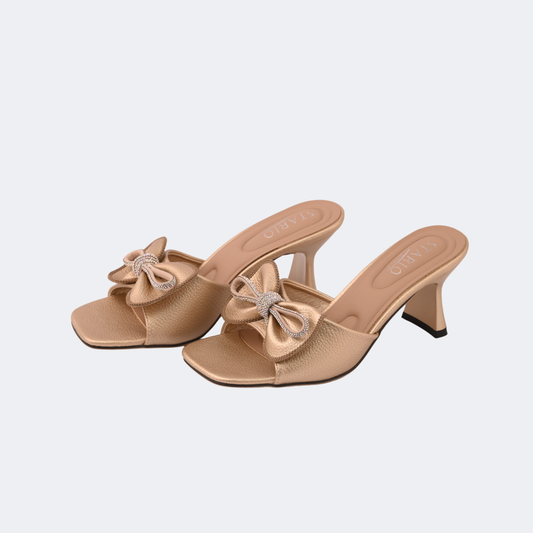 Pair of beige high-heeled shoes with bow details on a light gray background | Vogelle
