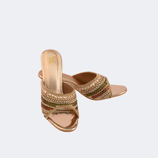 Pair of gold embellished high-heeled sandals on a light gray background | Vogelle