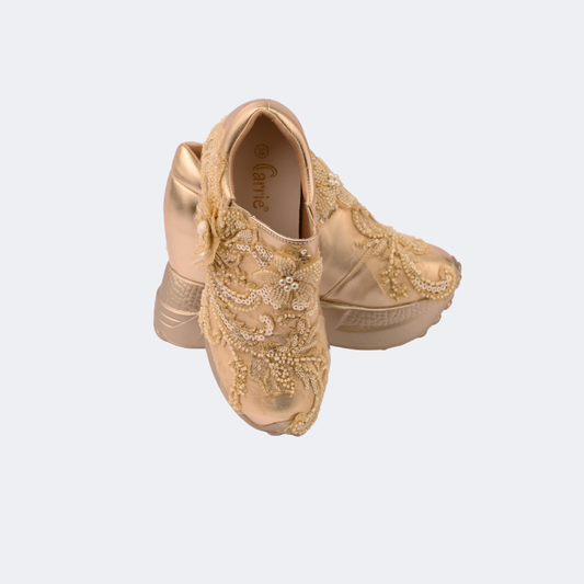 Pair of gold embellished shoes on a light gray background | Vogelle